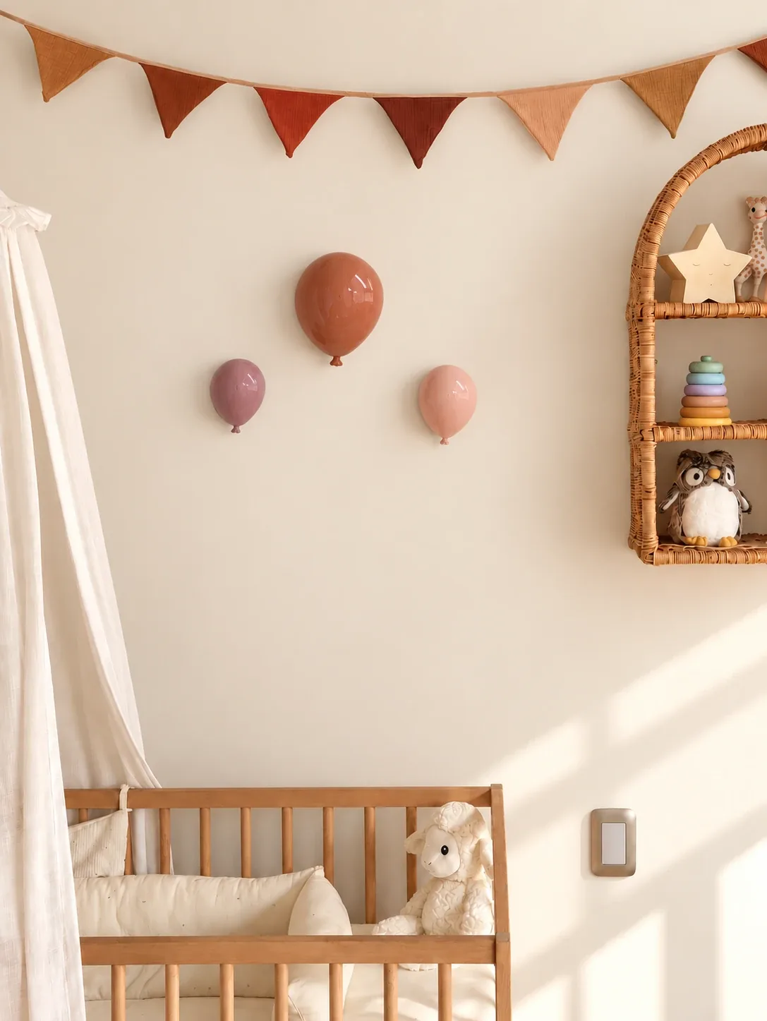Tres globos 3D en tonos terracota, ciruela y rosa sobre la pared de una pieza de bebé, junto a la cuna